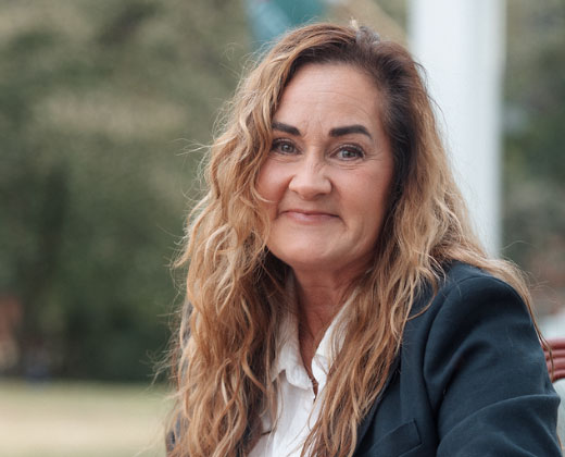 Headshot of Nora sitting in a chair, smiling on a porch with trees in the background